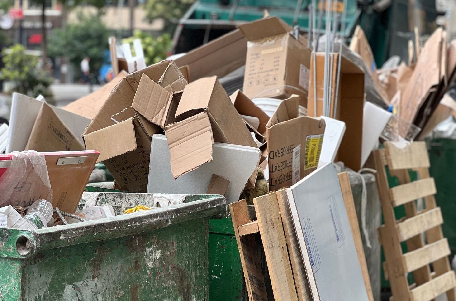 Piled cardboard boxes and waste in a city dumpster highlight urban recycling.