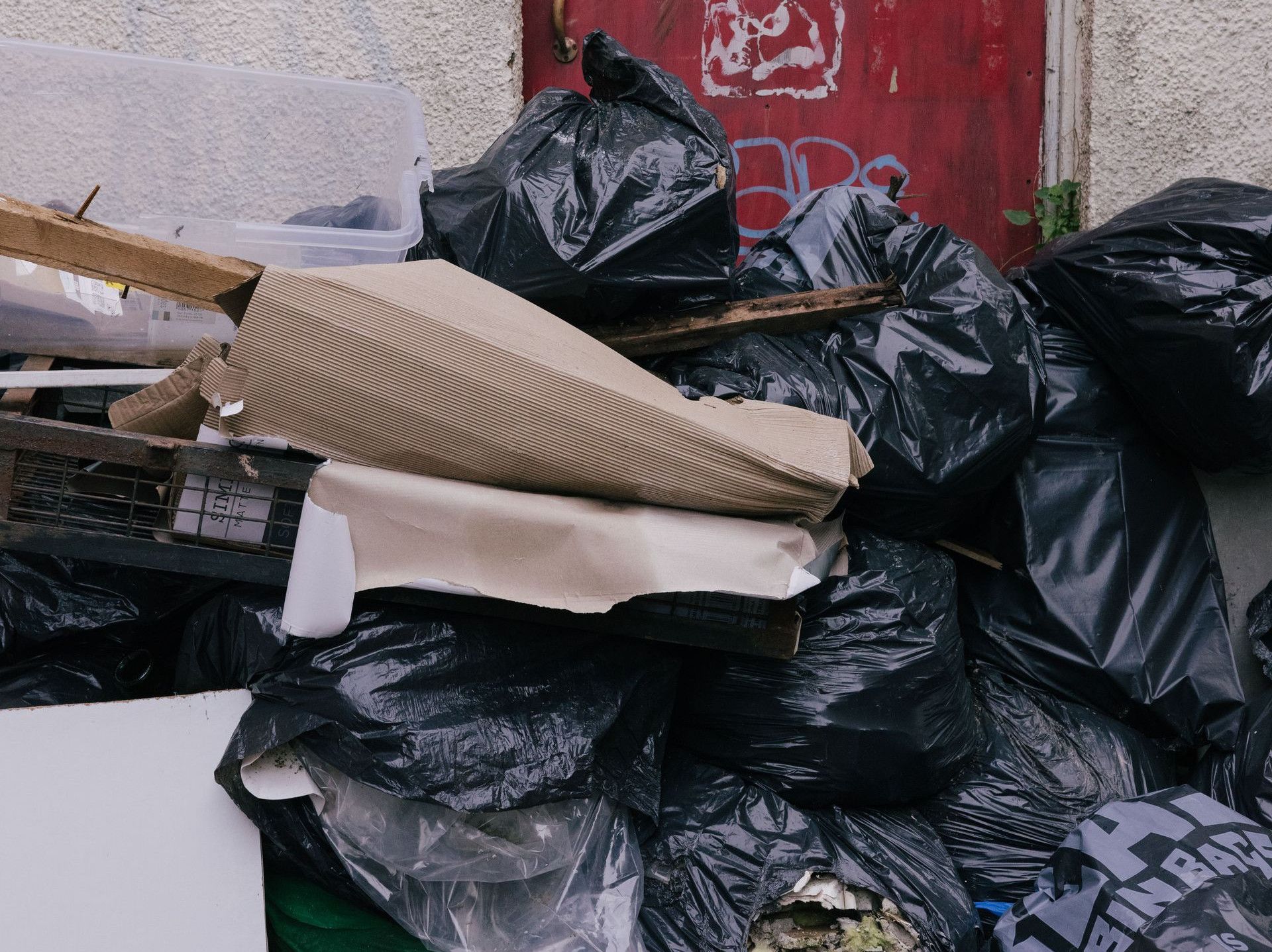 A pile of garbage in front of a graffiti-covered red door with urban decay elements.